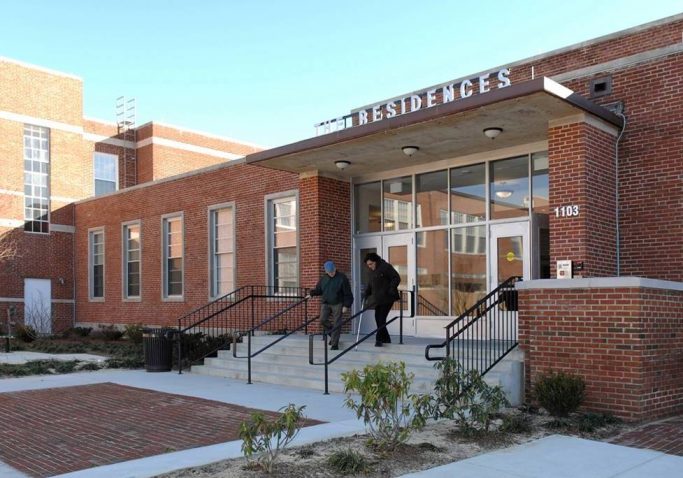 Two people walk down the steps outside a brick building labeled 