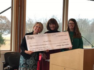 Three women smiling and holding a large ceremonial check from The Anne Arundel Association of REALTORS® for $1,500, dated December 14, 2018, awarded to The Light House. Trees and windows are visible in the background.