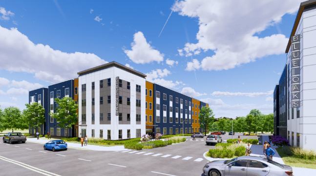 A modern, three-story apartment complex called Blue Oaks with colorful panels and large windows. People are walking and cars are parked in front, surrounded by green trees and landscaped areas on a sunny day.